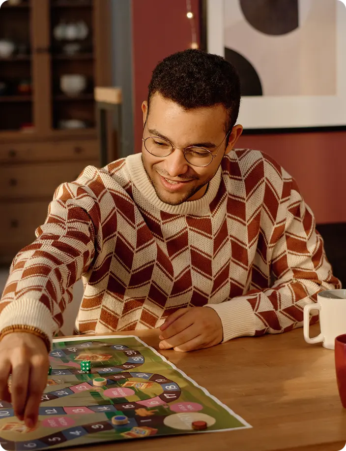 Een groep vrienden speelt een bordspel aan een houten tafel; ze zien er ontspannen uit en glimlachen. De warme verlichting en de informele kleding zorgen voor een gezellige, uitnodigende sfeer