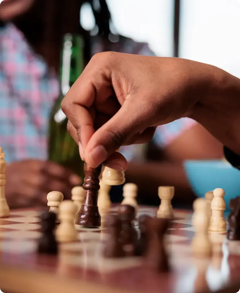 Twee mensen die schaken; één van hen verplaatst een wit paard. De scène straalt concentratie en strategisch inzicht uit, met een wazige achtergrond en warme tinten