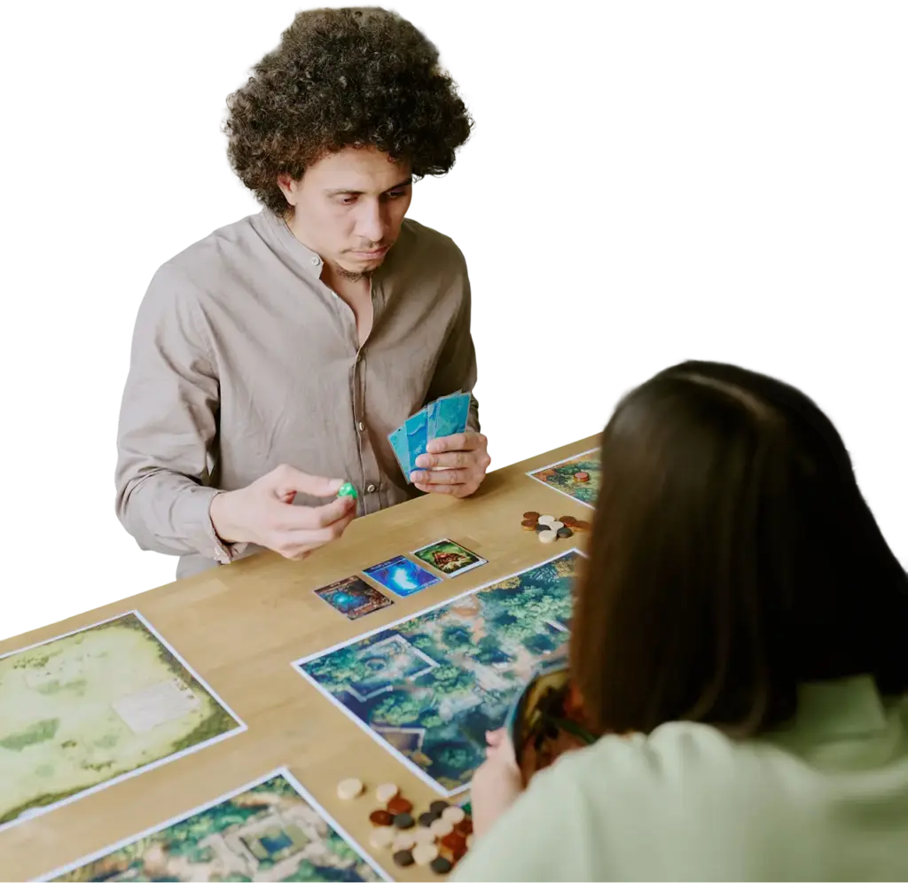 Een man en een vrouw spelen intensief een bordspel, waarbij kleurrijke kaarten en speelstukken over de tafel verspreid liggen. Op de achtergrond is een gezellige kamer te zien met planten en een blauwe bank